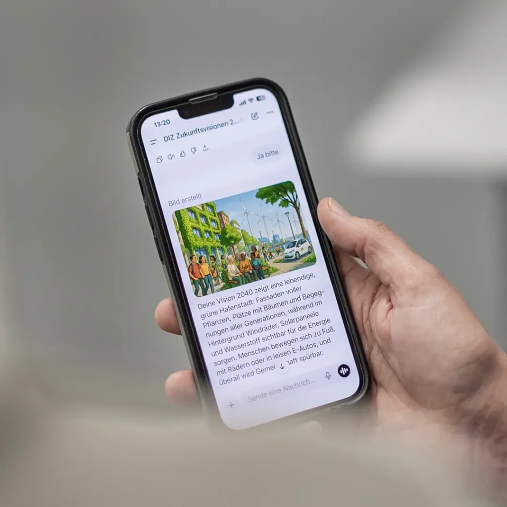 Hand hält ein Smartphone, auf dessen Display eine App eine bunte Illustration einer grünen Stadt mit Bäumen, Menschen, Windrädern und Elektroautos sowie begleitenden deutschen Text zur Vision 2040 zeigt.