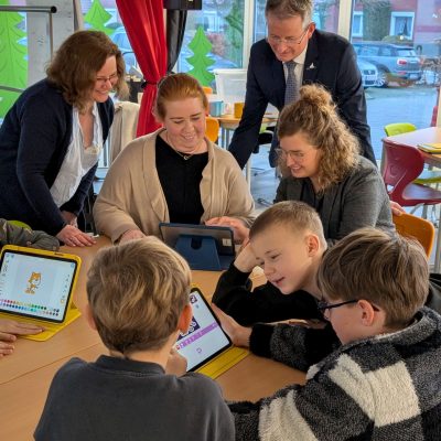 Digital Coachin Martina Schröder zeigt JadeBay-Geschäftsführerin Alexandra Wurm, Bürgermeister der Stadt Wittmund Rolf Claußen und Fachgebietsleiterin des Fachbereichs Personal und Kreisentwicklung beim Landkreis Wittmund Wiebke Börgmann das Programmiertool „ScratchJR.“, während die Schülerinnen und Schüler der dritten Klasse bereits fleißig damit programmieren üben.